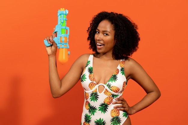 Speelse jonge zwarte vrouw in zwembroek met waterpistool