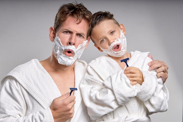 Speelse man en kleine jongen die plezier hebben met scheerschuim op gezichten in geïsoleerde badkamer