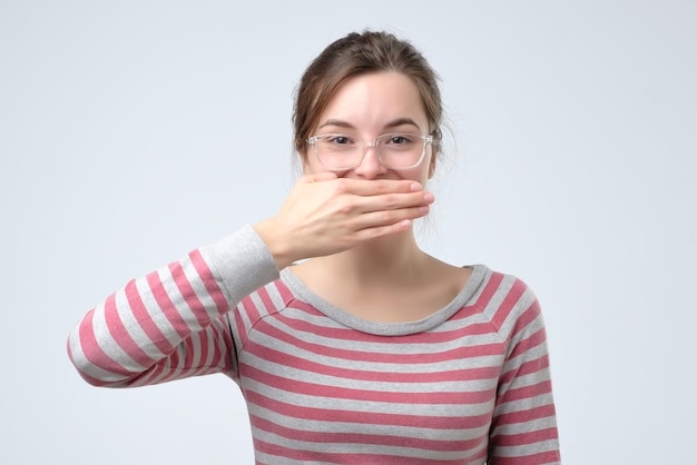 Speelse mooie vrouw die haar gezicht verbergt en timide lacht