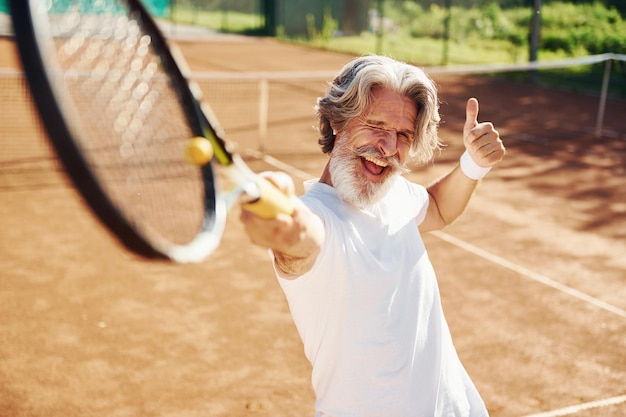 Speelspel Senior moderne stijlvolle man met racket buitenshuis op tennisbaan overdag