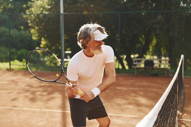 Speelspel Senior moderne stijlvolle man met racket buitenshuis op tennisbaan overdag