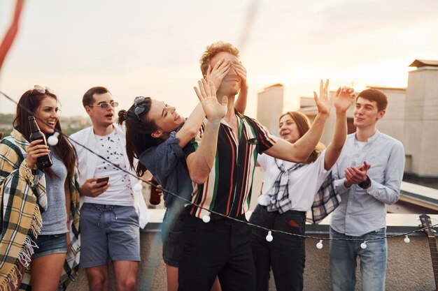 Spel spelen Man's ogen bedekt met handen Groep jonge mensen in vrijetijdskleding hebben overdag samen een feestje op het dak