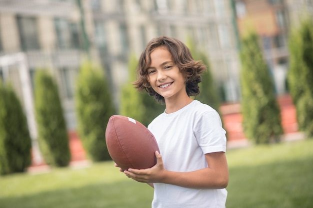 Spelen. Donkerharige jongen in een witte t-shirt spelen met een bal