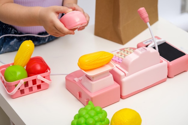 Spelen in de winkel kinderhand scant en weegt groenten maïs op speelgoedweegschalen kinderkassa close-up kinder home games concept
