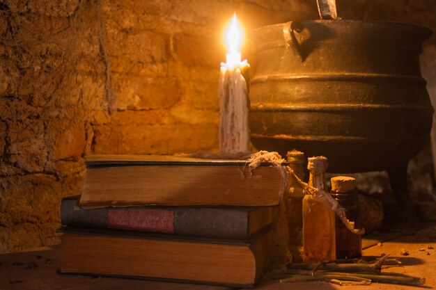 Incantesimo della notte delle streghe con candele e pentola con il fuoco tra ragnatele e terra antica