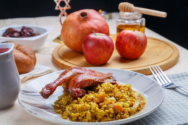 Foto spelt met een eendenpoot in een bord op de feesttafel voor rosh hashanah naast granaten grijze appels wijn en challah