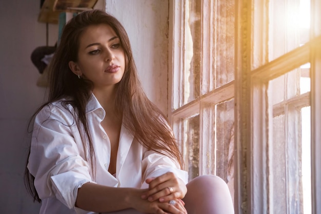 Trascorri del tempo a casa accogliente ritratto carino triste giovane donna in camicia bianca pensiero profondo