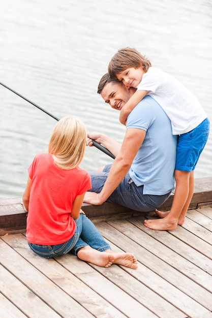 Spending great time together. Happy father fishing with his kids while sitting at the riverbank together