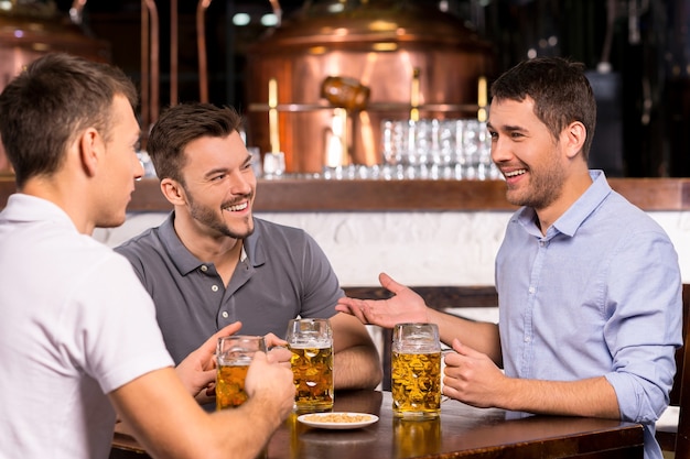 Spending time in bar. Three cheerful friends drinking beer in bar