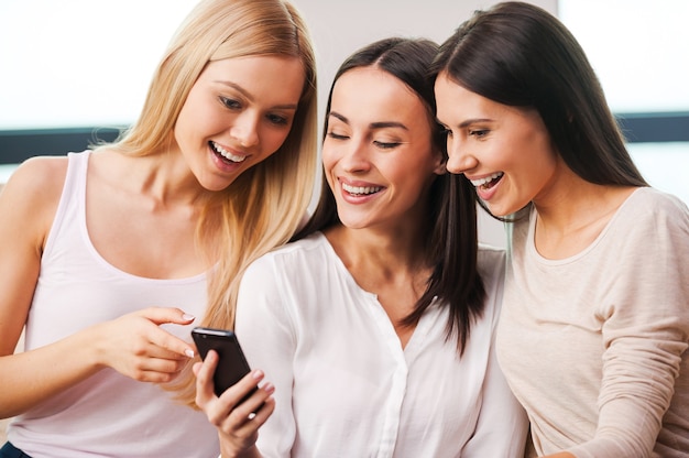 Spending time with friends. Three beautiful young women looking at the mobile phone and smiling 