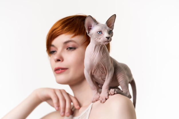 Sphynx hairless kitten sitting on shoulder of pretty redhead young woman with short hair head shot