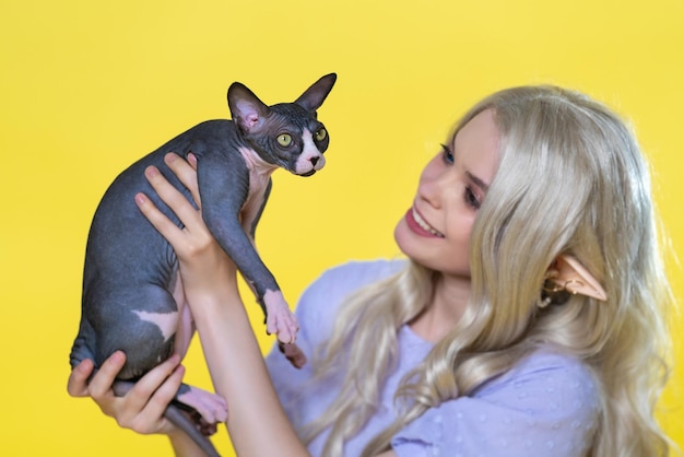 スフィンクスの子猫と若い金の女性が黄色い背景でコスプレしている