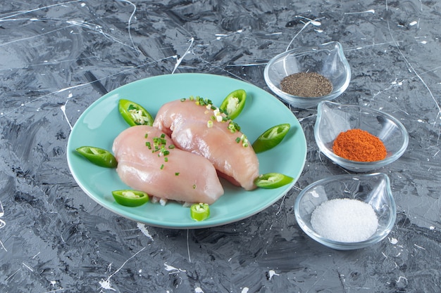 Spice bowls and chicken breast on a plate , on the marble surface.