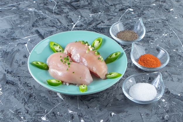 Ciotole di spezie e petto di pollo su un piatto, sulla superficie di marmo.