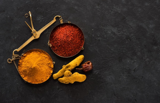 Spice turmeric root and chili pepper, and turmeric powder and chili powder on brass scales, top view and copy space for text