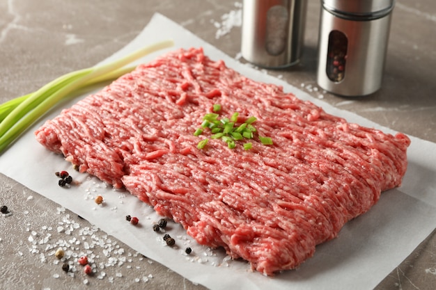 Spices and baking paper with minced meat on grey, close up