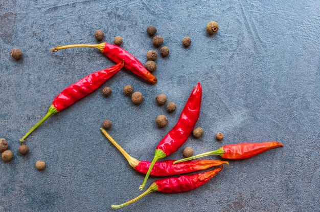 Spices of black pepper and red hot pepper lie on a cutting board made of dark stone