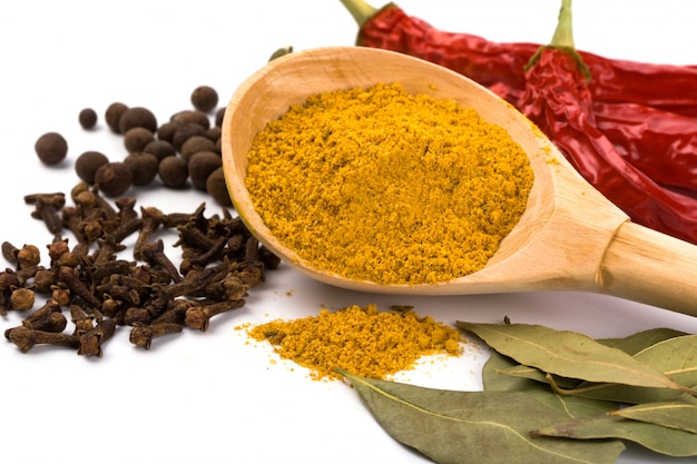 Spices: curry in wooden spoon, pepper, pimento, cloves and bay leaves on white background