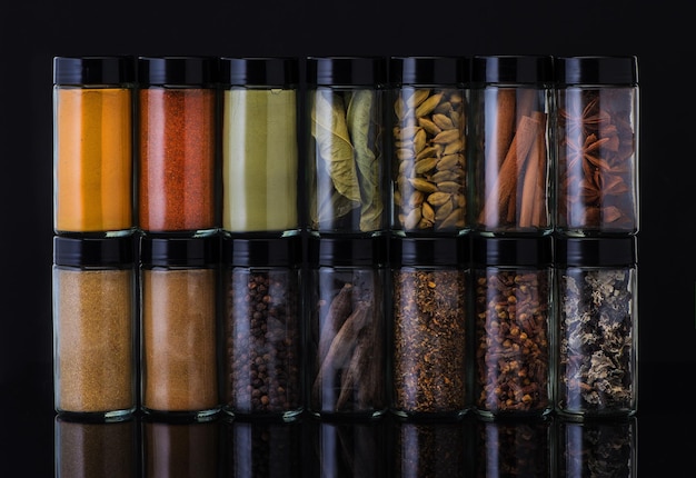 Spices in glass jars on a black background Spicy and seasonings Food and cooking background