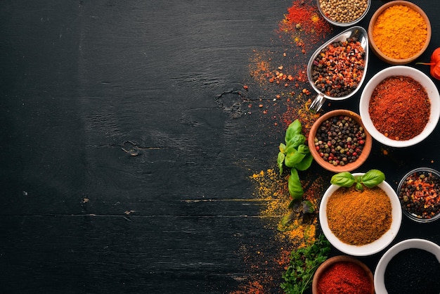 Spices and herbs on a wooden board Pepper salt paprika basil turmeric On a black wooden chalkboard Top view Free copy space