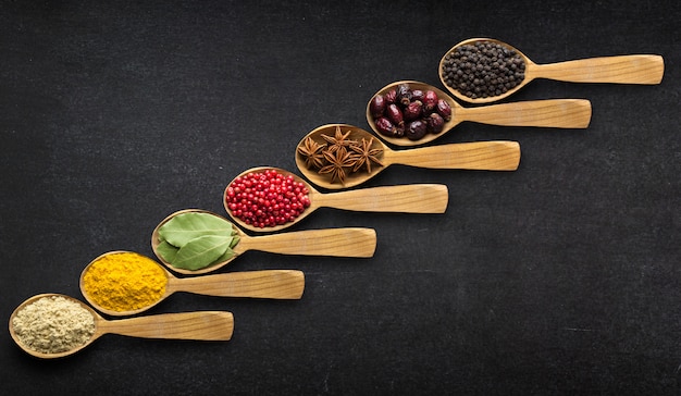 Spices in spoons over black table background. Top view of season