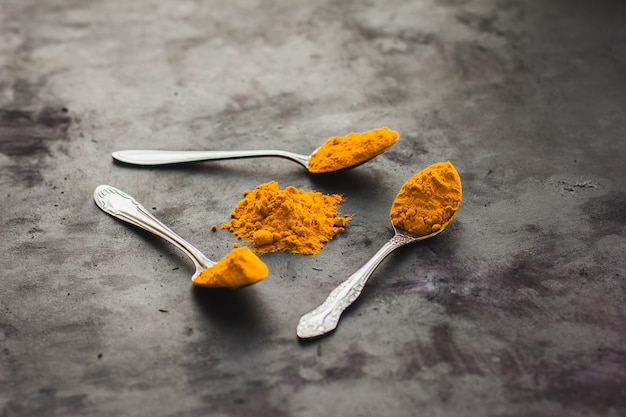 Spices turmeric in a spoon on a dark background, seasonings and healthy food