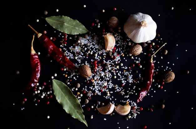 Spices white black and red peppers sea salt sprinkled garlic
and chilli on a black background closeup