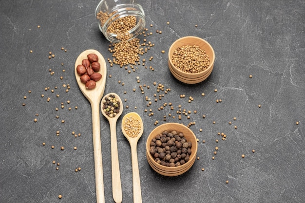 Spices in wooden spoons Coriander seeds in glass jar Allspice in wooden bowl Copy space Flat lay Black background