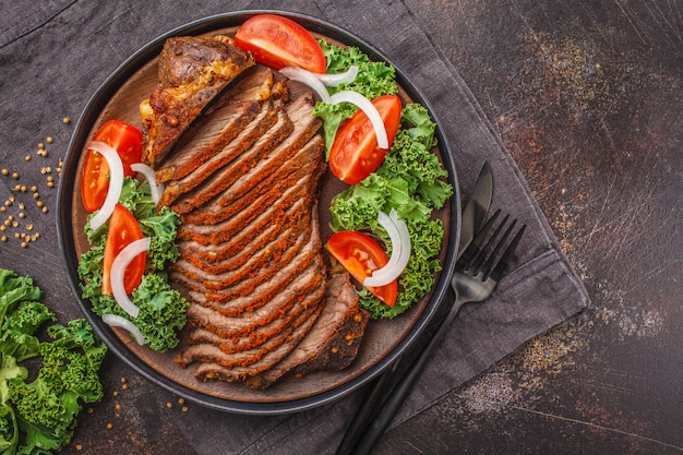 Spicy baked beef with kale salad in black plate on dark background.