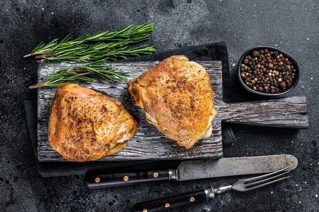 Cosce di pollo alla griglia piccante barbecue su una tavola di legno con rosmarino. sfondo nero. vista dall'alto.