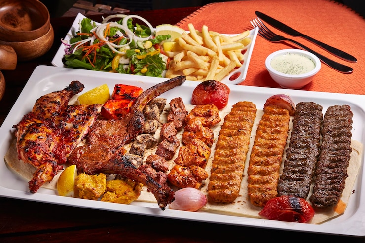 スパイシーなバーベキュー ミックス グリル盛り合わせティッカ ボティ kababs フライド ポテト サラダとライタ中東食品のテーブル サイド ビューに分離された皿で提供しています