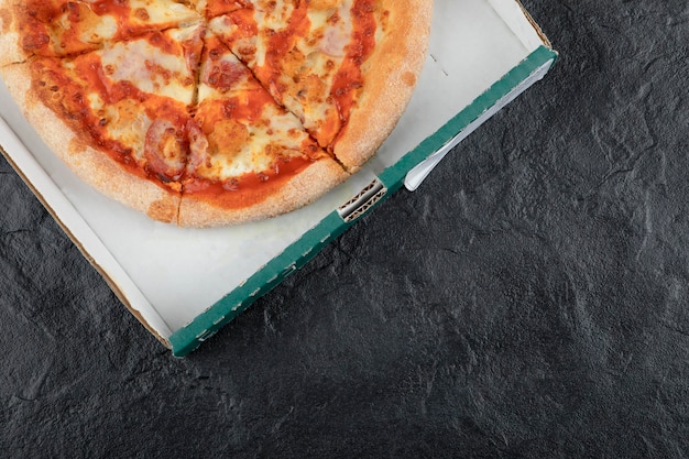 Spicy buffalo chicken pizza in carton box on black surface.