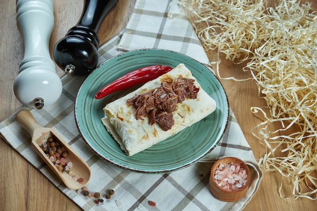 Burrito piccante o shawarma su un piatto blu con manzo tradizionale bollito e morbido in una composizione con spezie. vista da vicino. foto di cibo. disteso