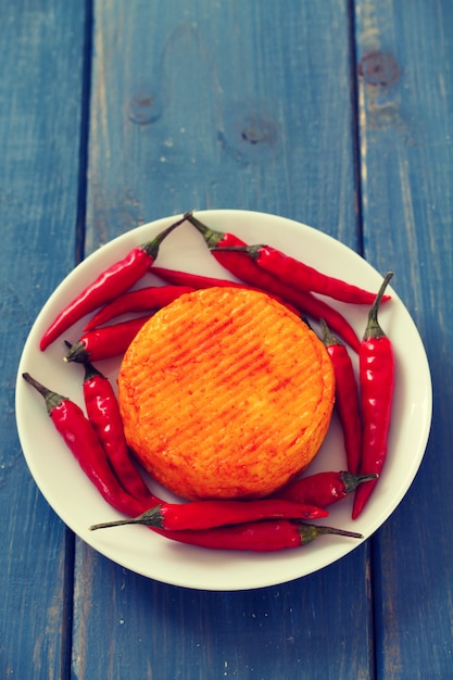 Spicy cheese with red pepper on white plate on blue wooden surface