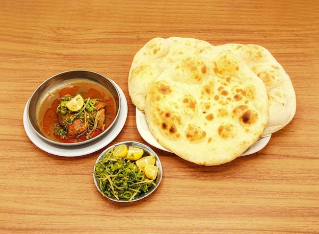 スパイシー チキン コルマ カミリ ロティ レモン スライスとサラダは、インドのパキスタン料理の木製のテーブルの側面図に分離された皿で提供しています