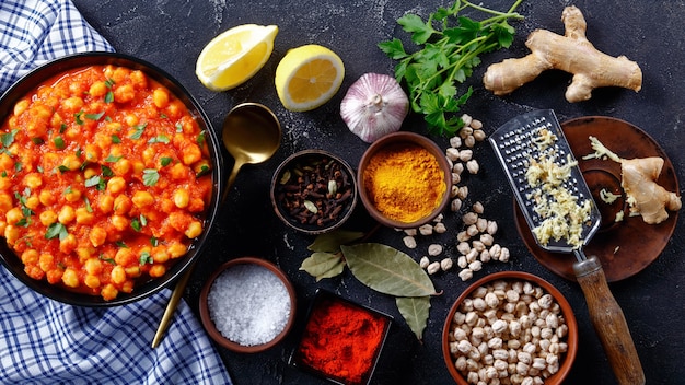 Photo spicy chickpea curry with ingredients on a dark concrete background: