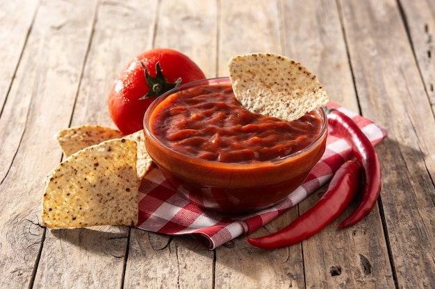 Spicy chili sauce in bowl with nacho chips on wooden table