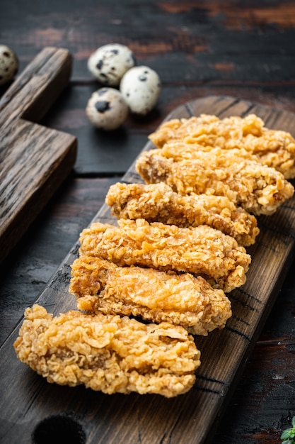 Spicy deep fried breaded chicken wings cuts on dark wooden table.