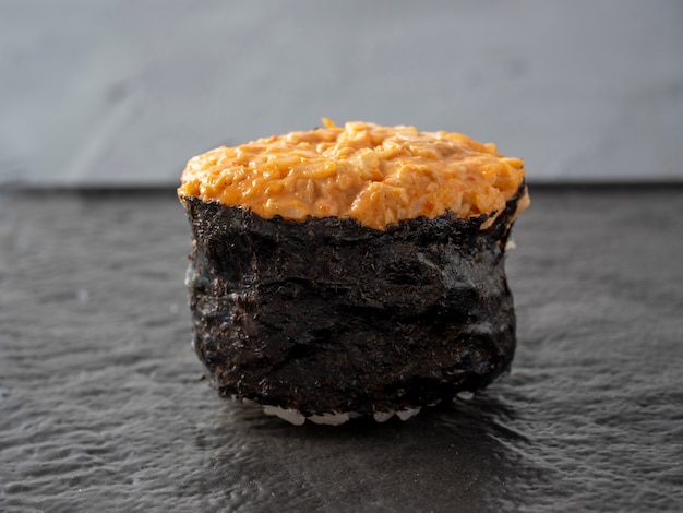 Фото Острый гункан с курицей и острым соусом на темной текстурированной поверхности. вид сбоку