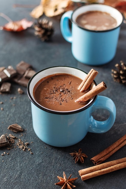 Spicy hot chocolate with cinnamon and star anise in enamel blue mugs on black background