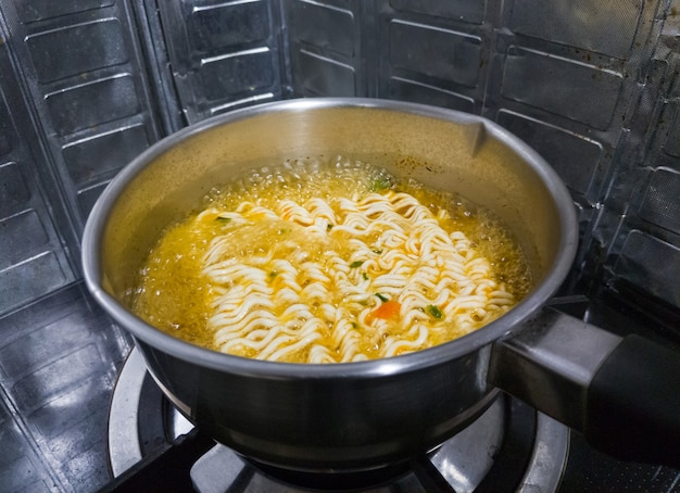 Gli spaghetti istantanei piccanti stanno bollendo in una pentola di metallo su un fornello a gas nella cucina della casa urbana per pranzo, vista frontale per lo sfondo.