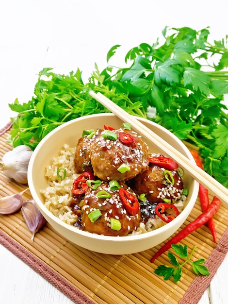 Spicy Korean meatballs in sauce of starch soy sauce vinegar and apricot jam sprinkled with green onions hot peppers and sesame seeds in a bowl on a bamboo napkin against wooden board background