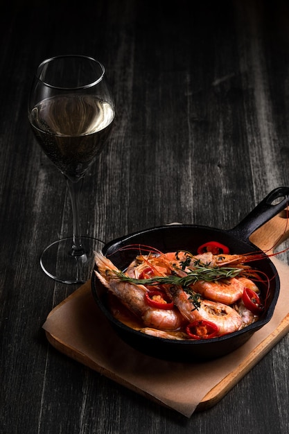 Spicy langoustines with pepper and rosemary in a frying pan served with a glass of wine