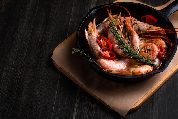 Photo spicy langoustines with pepper and rosemary in a frying pan served with a glass of wine