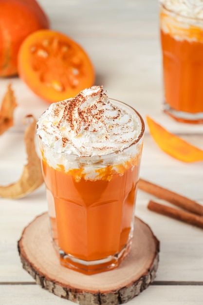 Latte piccante con zucca e panna montata su fondo in legno caffè caldo in tazza di vetro e foglie autunnali