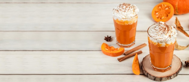Spicy latte with pumpkin and whipped cream on wooden background Hot coffee in glass mug and autumn leaves