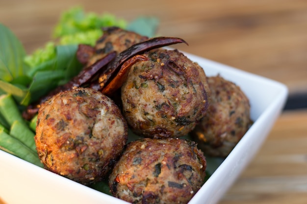 Spicy mince pork balls with salad in a white plate on the table. Thai food (Larb Moo Tod)