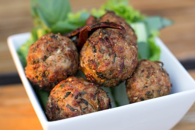 Le spezie piccanti tritano le palle di maiale con insalata in un piatto bianco sul tavolo. cibo tailandese (larb moo tod)