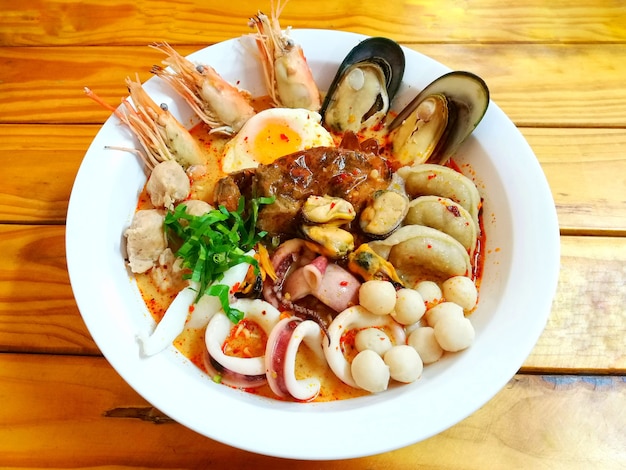 Spicy noodle with seafood and stream egg in white bowl on wooden table