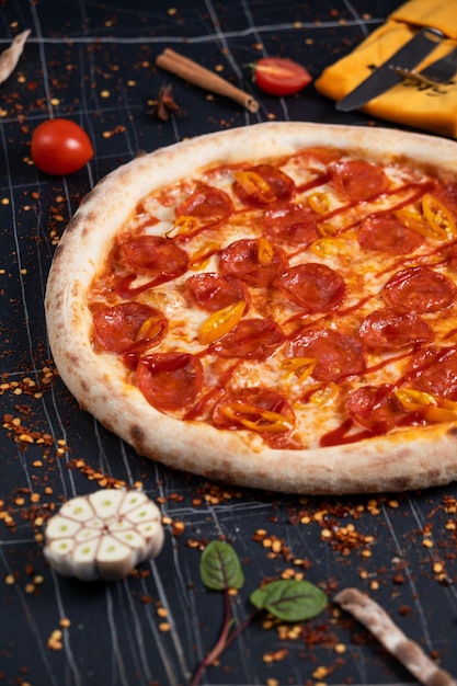 Spicy pizza with sausages and chili peppers On a black stone background Free space for text